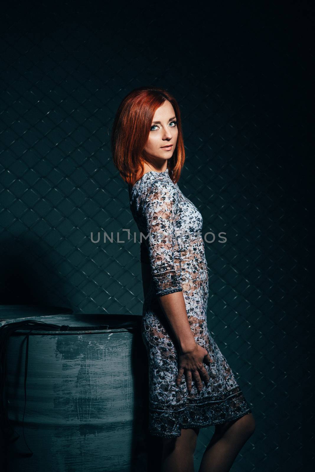 redheaded model girl in a long dress in a dark industrial Studio near barrels of oil