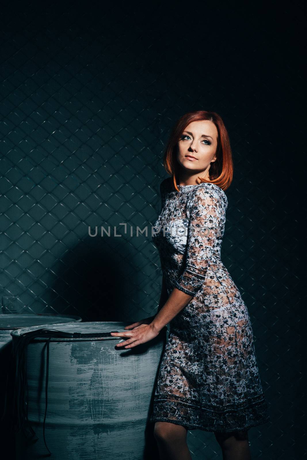 redheaded model girl in a long dress in a dark industrial Studio near barrels of oil