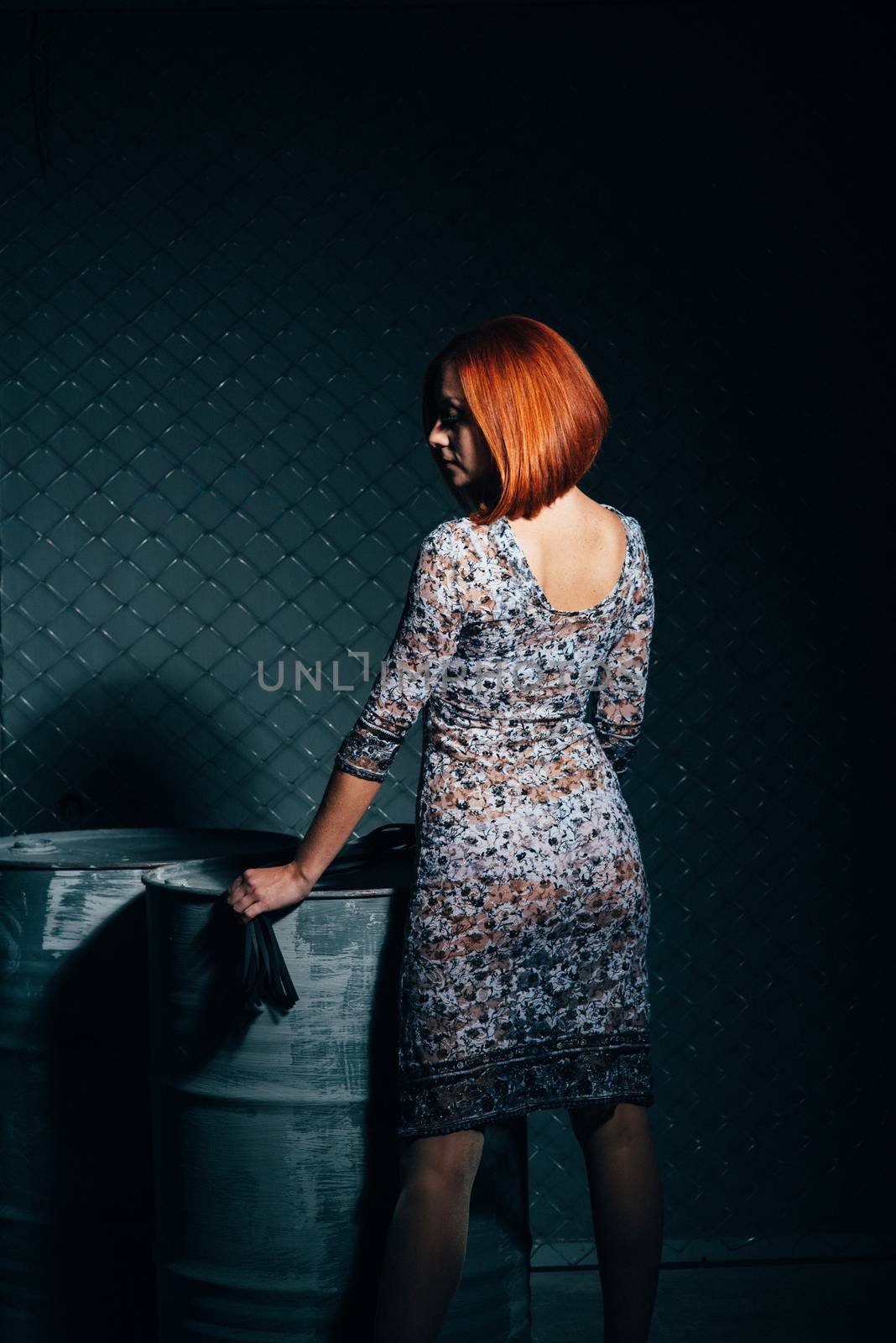redheaded model girl in a long dress in a dark industrial Studio near barrels of oil
