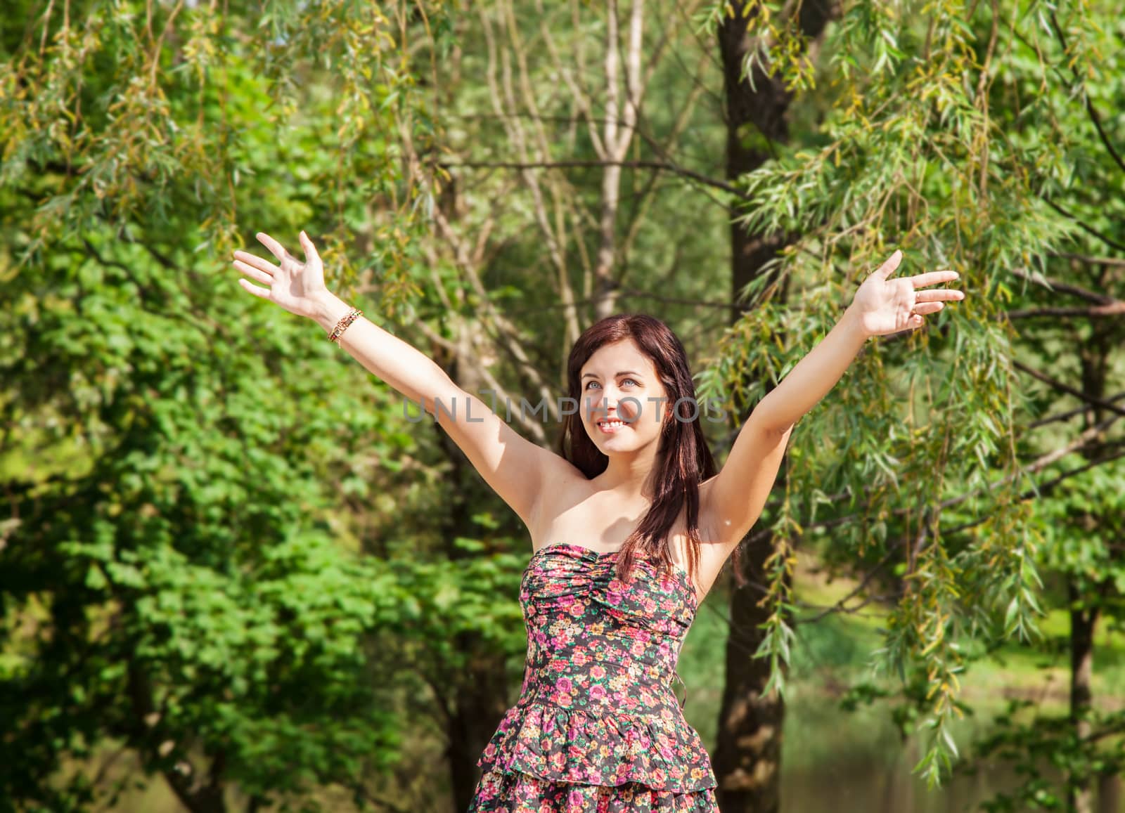 young beautiful smiling girl holds out her hands to the sky in the park on summer day