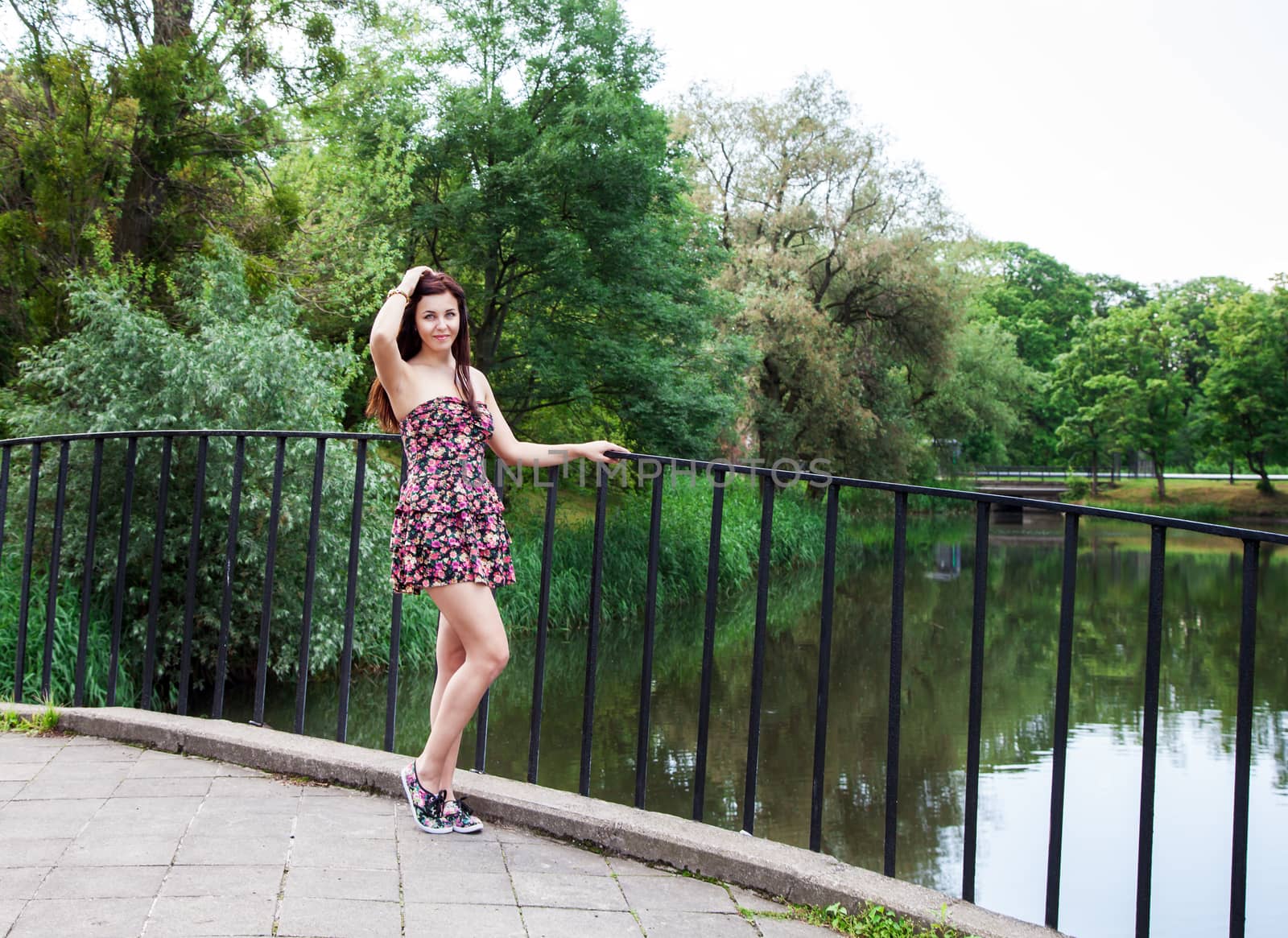 young beautiful brunette standing on the bridge near the river on summer day