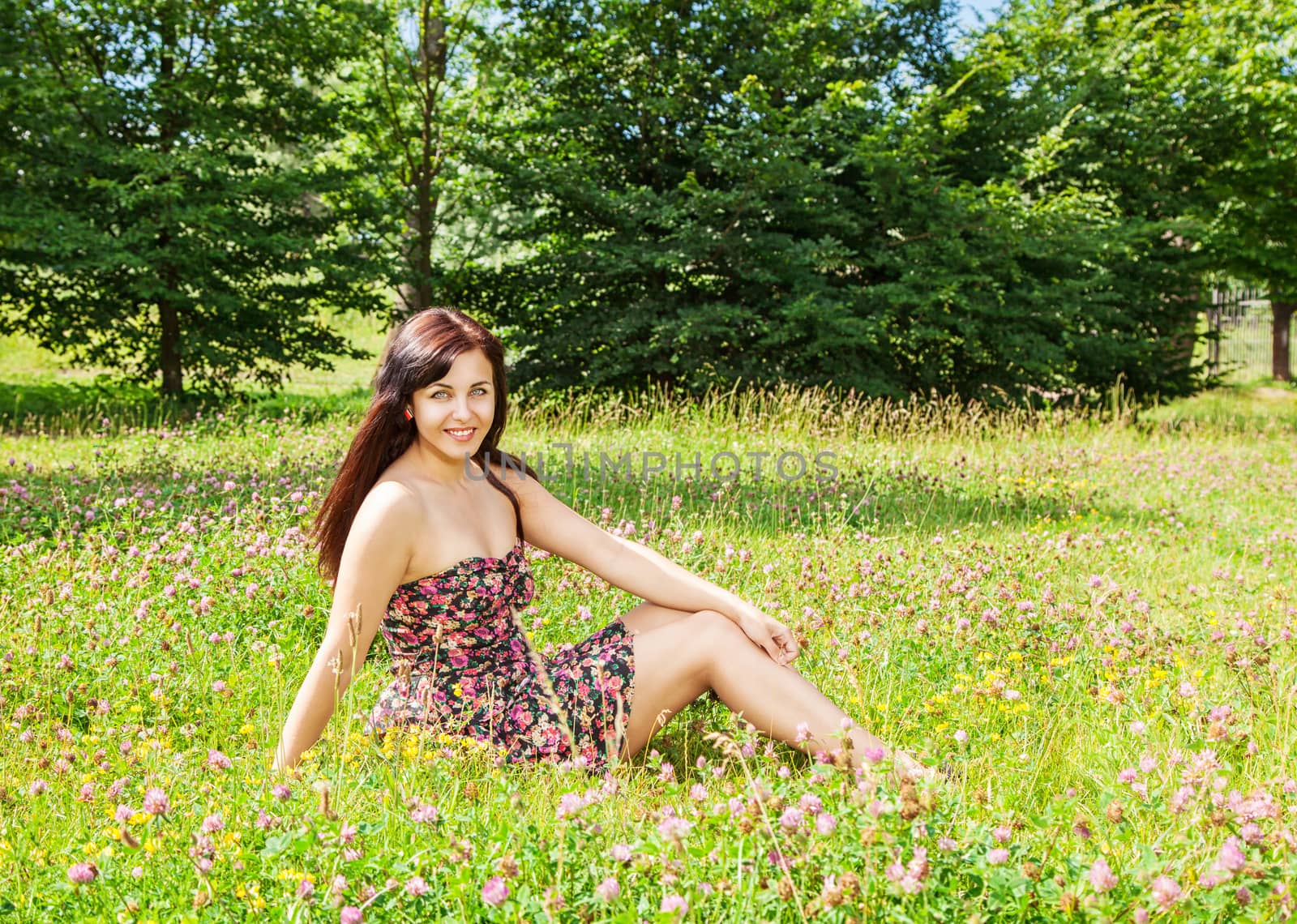 young beautiful brunette sitting on the grass in a city park on sunny summer day