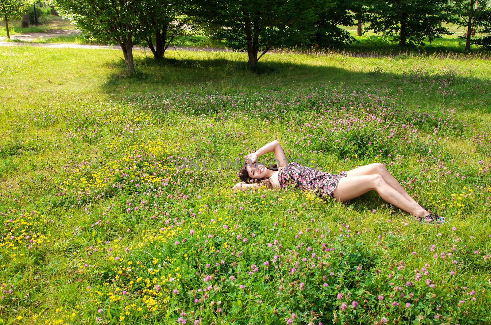 young beautiful brunette lying on the grass in a city park on sunny summer day