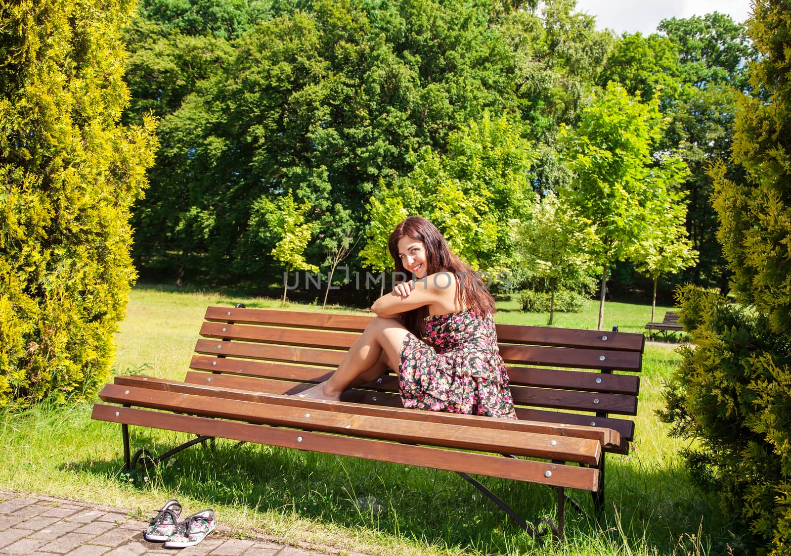 young beautiful smiling girl girl sitting on a park bench on sunny summer day