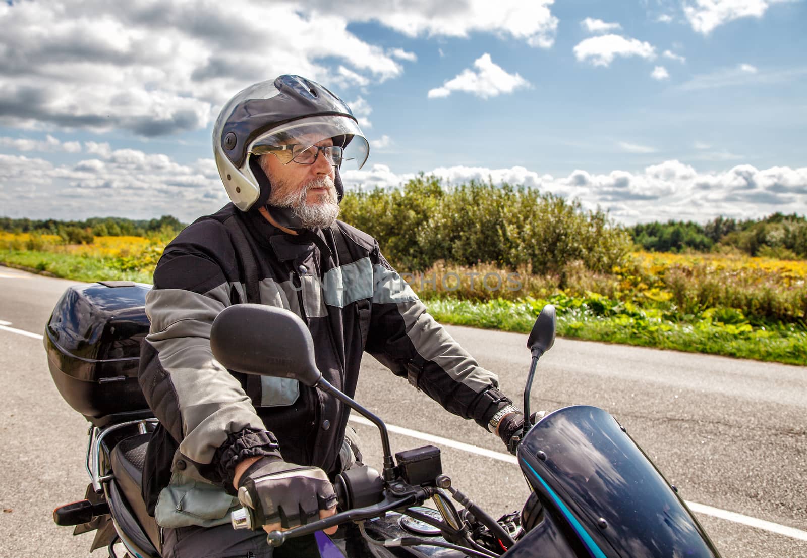 elderly motorcyclist wearing a jacket and glasses with a helmet sitting on his motorcycle on the road