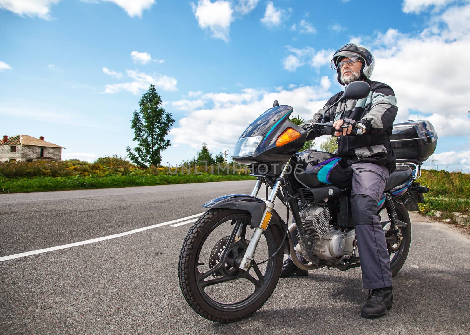 elderly motorcyclist wearing a jacket and glasses with a helmet sitting on his motorcycle on the open road