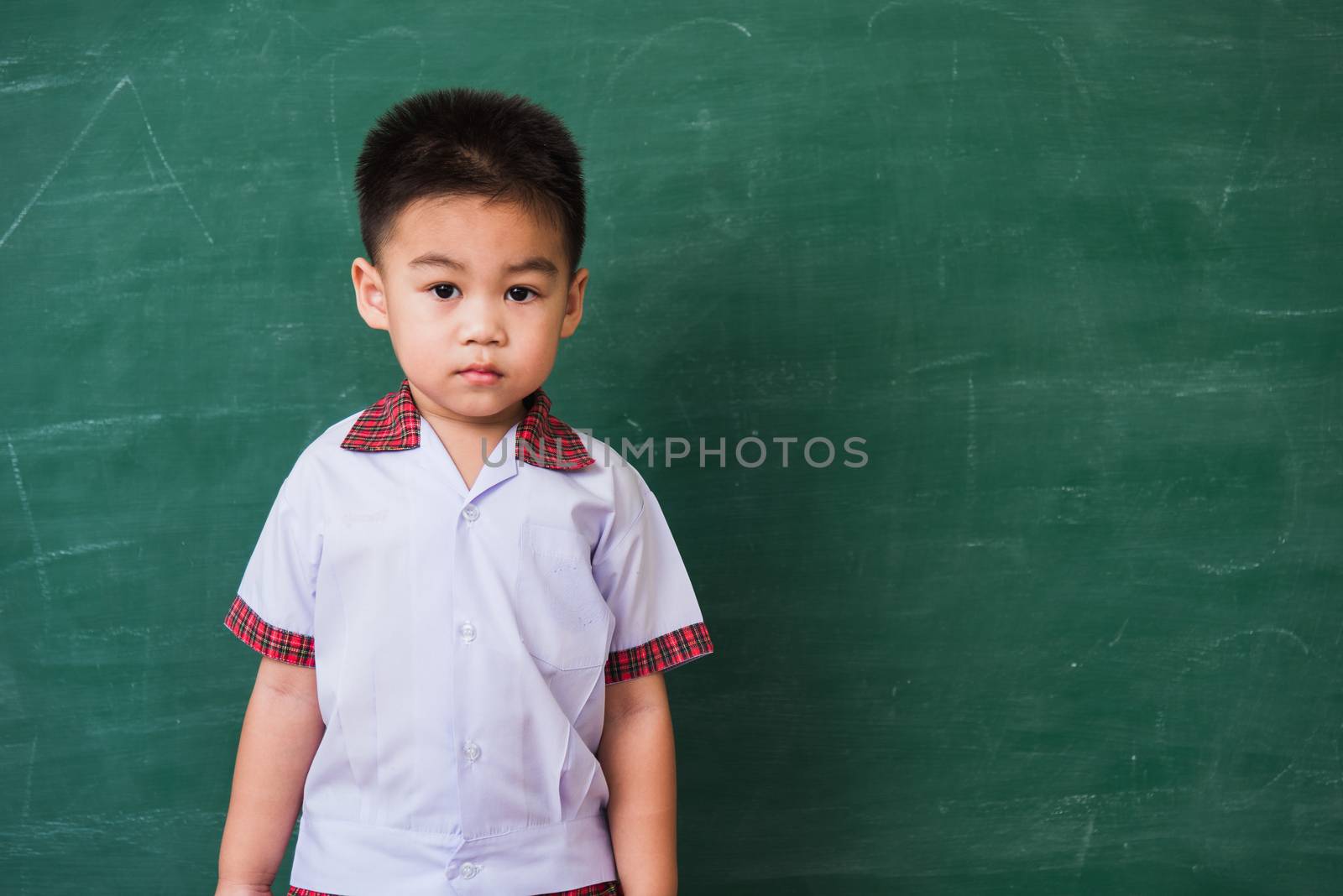 Back to School. Happy Asian funny cute little child boy from kindergarten in student uniform smiling on green school blackboard, First time to school education concept, studio shot