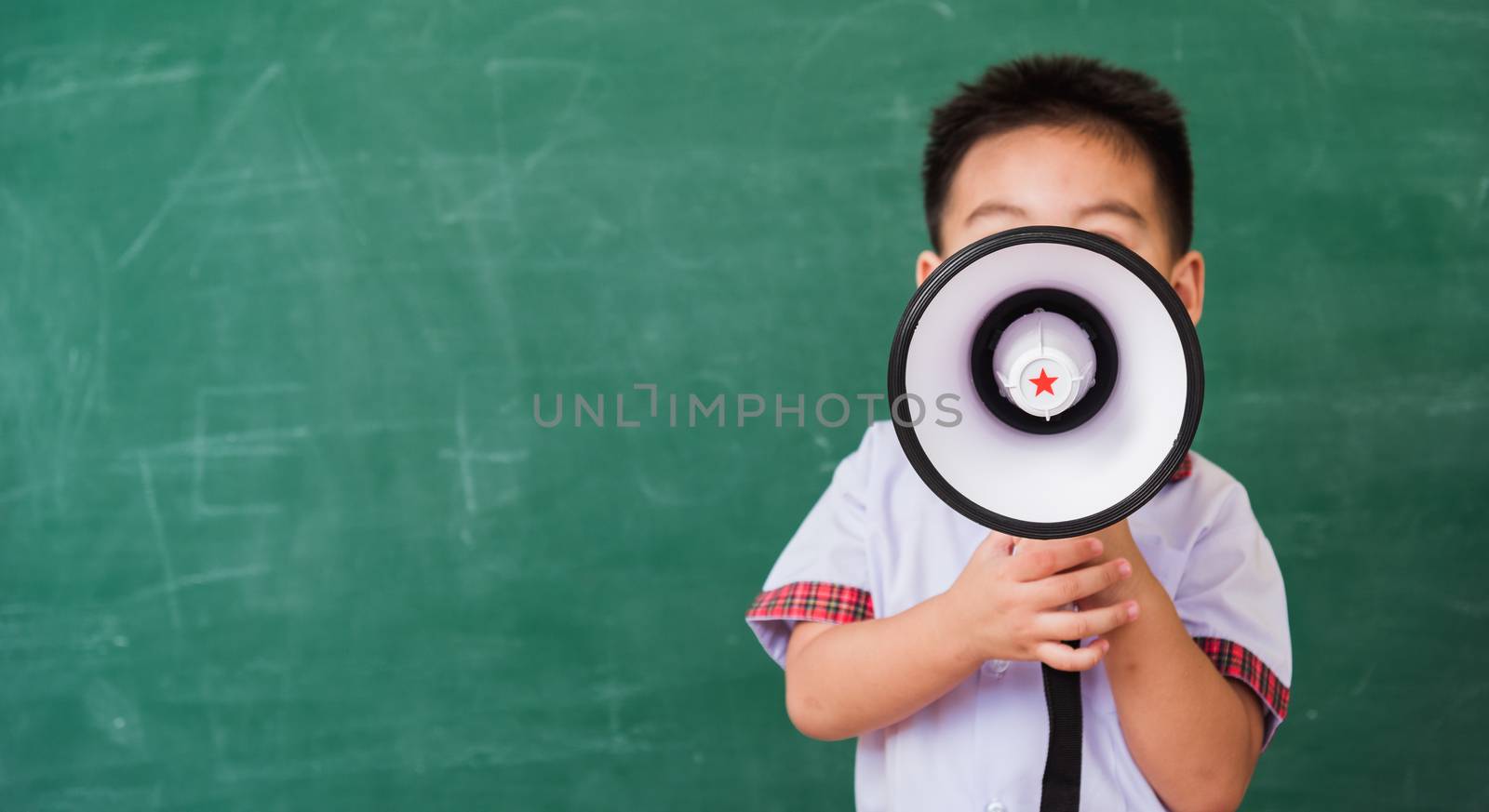 Back to School. Asian funny cute little child boy kindergarten preschool in student uniform speaking through megaphone against on green school blackboard, First time to school education concept