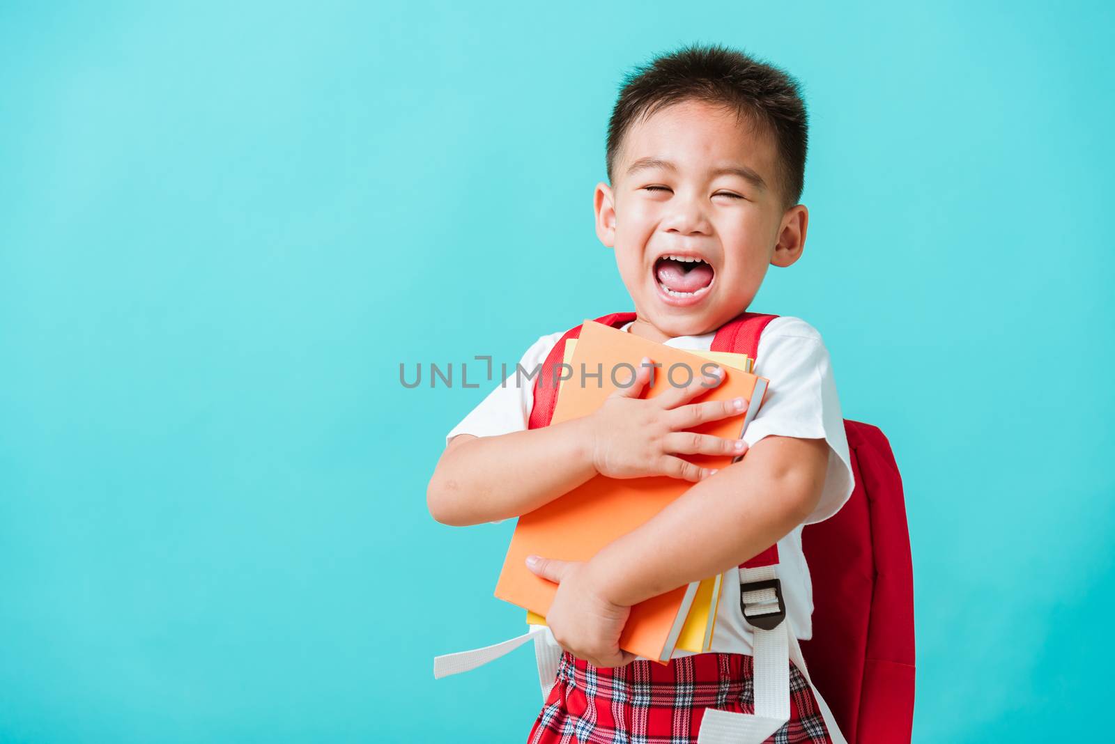 Back to school concept. Portrait Asian happy funny cute little child boy smiling and laugh hug books, studio shot isolated blue background. Kid from preschool kindergarten with school bag education