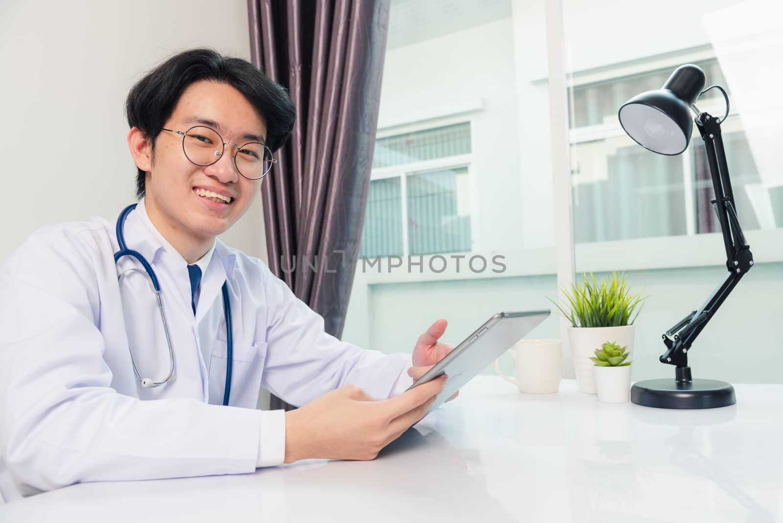 Happy Asian young doctor handsome man smile work from home office wear glasses, using black modern smart digital tablet computer on desk at hospital office, Technology healthcare and medicine concept