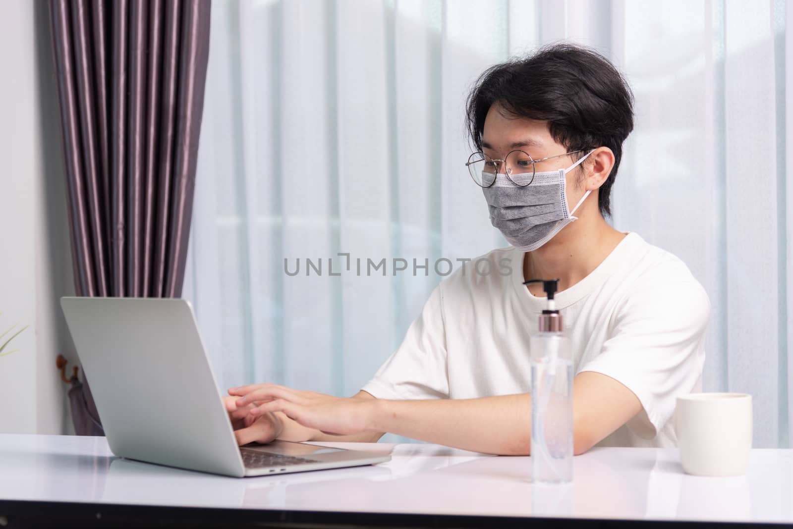 young man wearing a protective mask with disinfectant gel beside by Sorapop