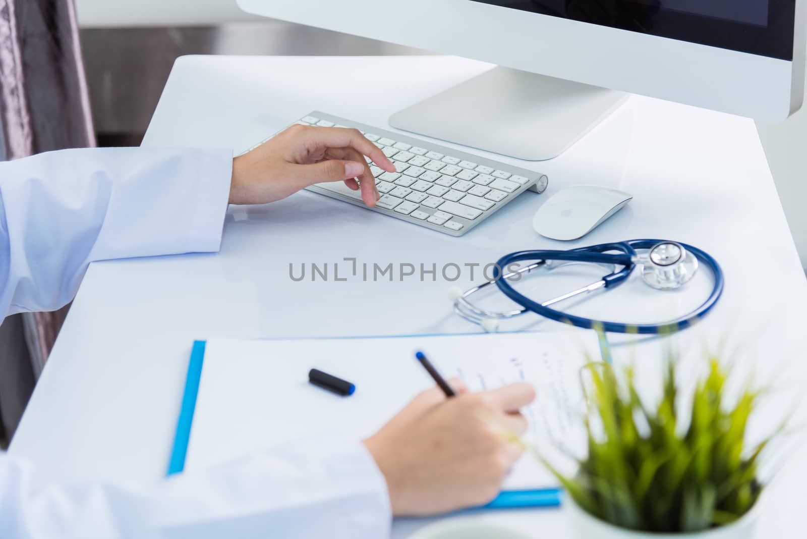 Medicine doctor's working on desk. Closeup of Stethoscope. Hand of Asian woman physician writing record patient information on paper note front PC computer at hospital office, Healthcare medic concept