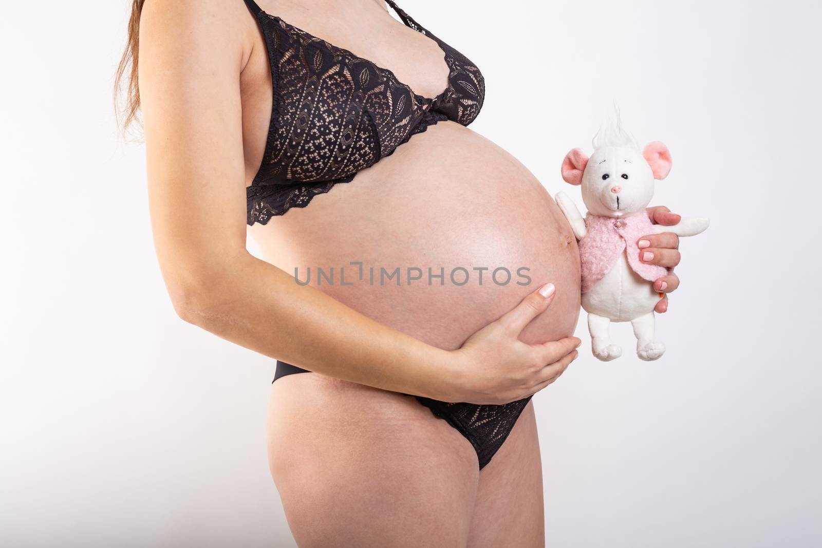 Close-up pregnant woman's belly with mouse toy. Beautiful pregnant woman. Pregnancy, parenthood, preparation and expectation concept. by Vassiliy
