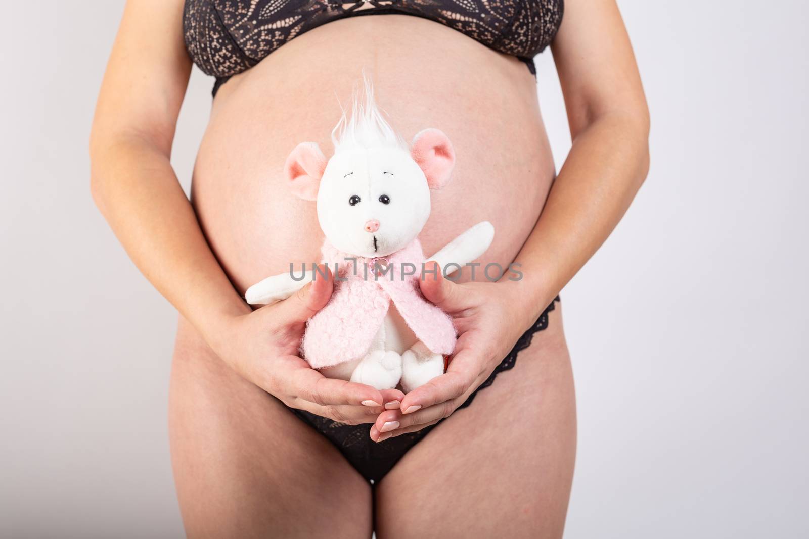 Close-up pregnant woman's belly with mouse toy. Beautiful pregnant woman. Pregnancy, parenthood, preparation and expectation concept. by Vassiliy