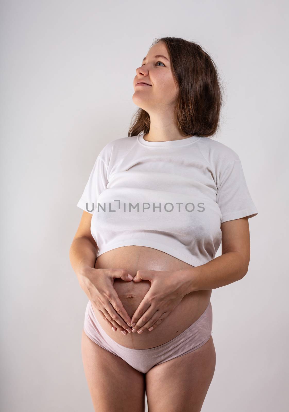 Young beautiful pregnant woman with long healthy curly hair posing in black underwear on grey background. Active pregnancy