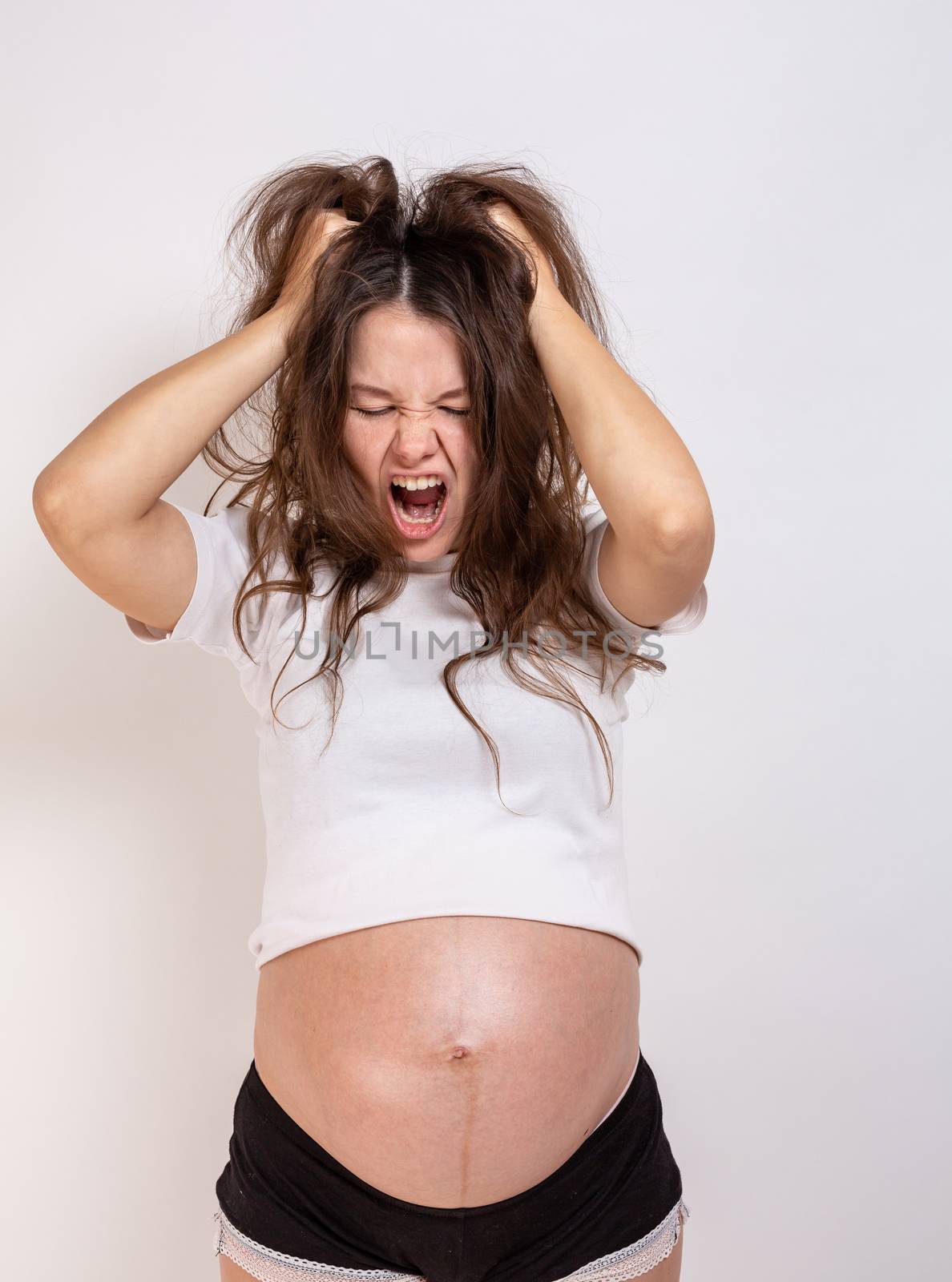 The young beautiful pregnant woman experiences strong emotions on a white background by Vassiliy
