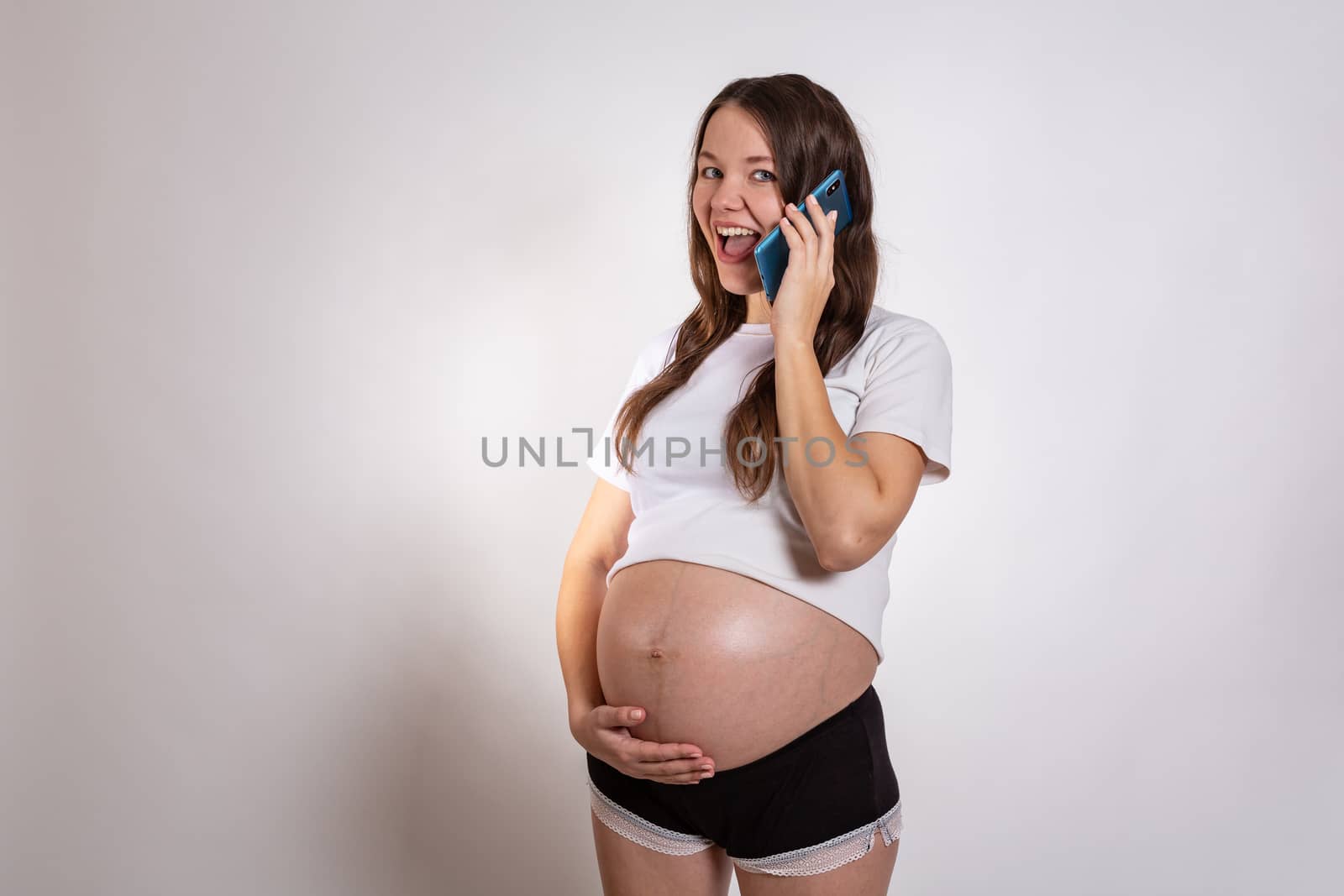 Cute pregnant woman on the phone while lying on a white background.