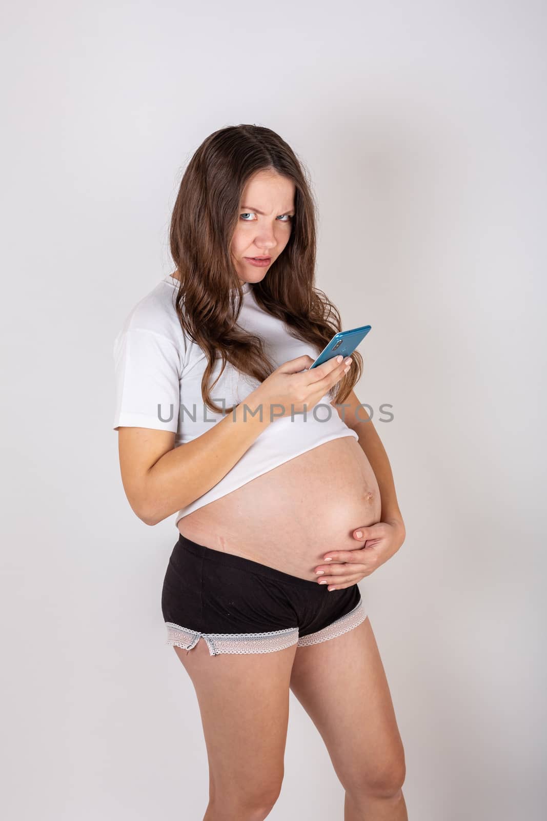 Cute pregnant woman on the phone while lying on a white background.