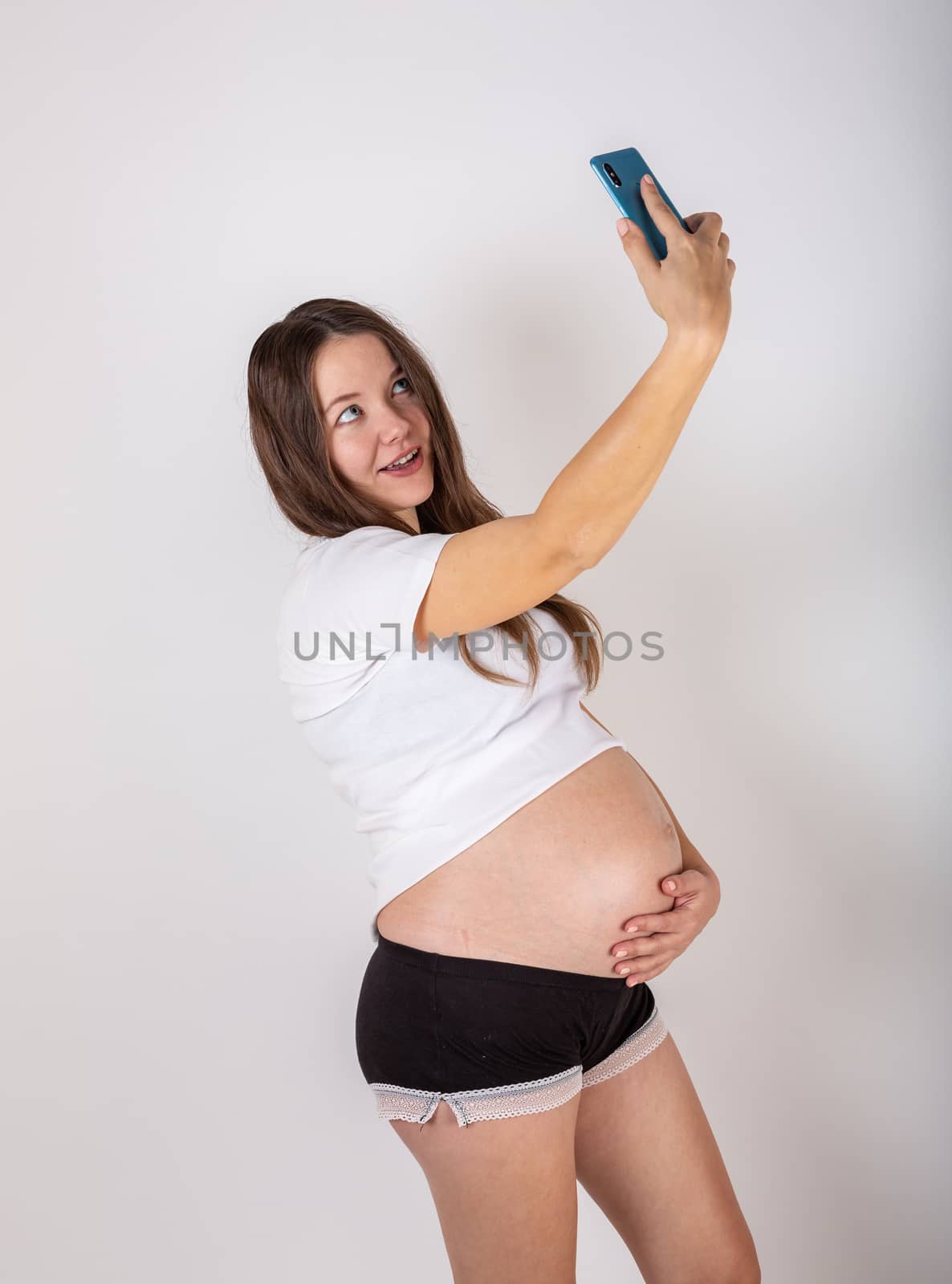 Cute pregnant woman on the phone while lying on a white background.