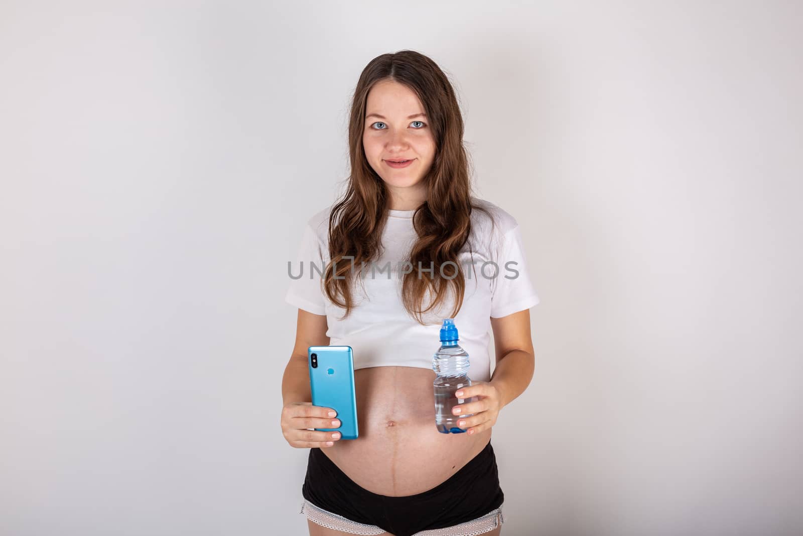 beautiful pregnant brunette woman drinking water from the bottle on isolated white background.