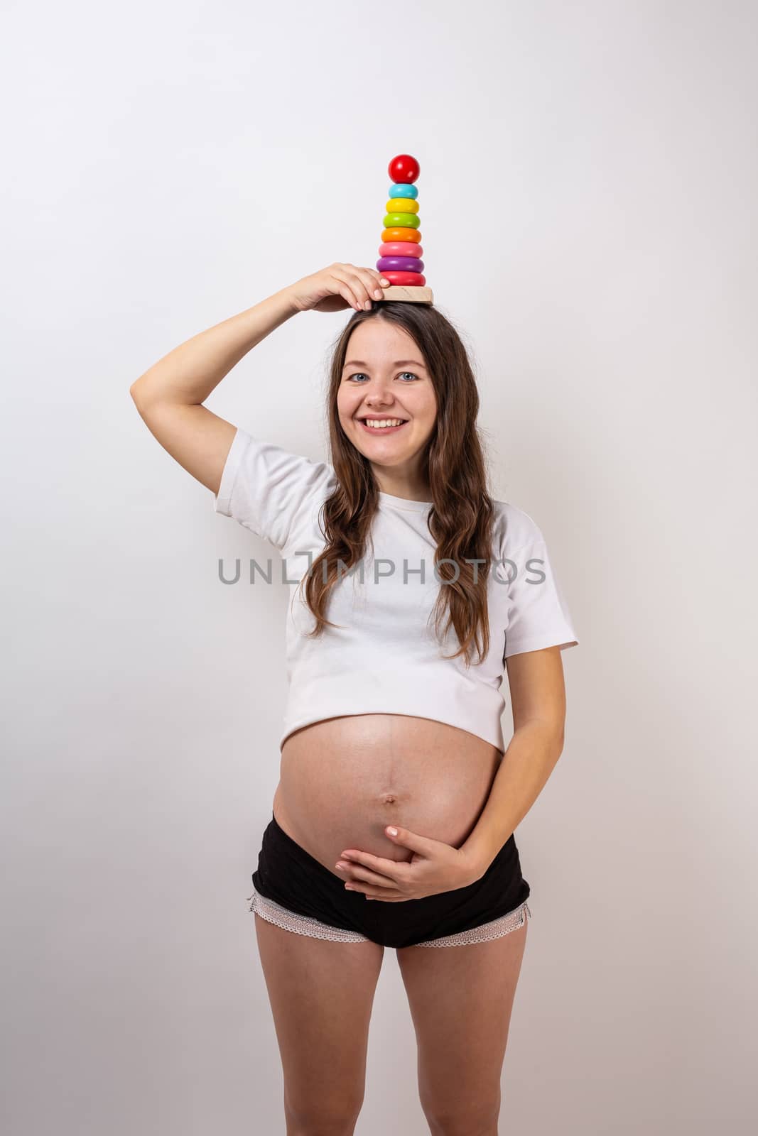 Pregnant girl with a wooden rainbow pyramid for children.