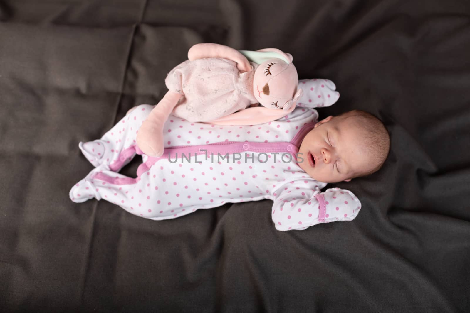 pretty smiling baby girl and toy rabbit lying in darck background.