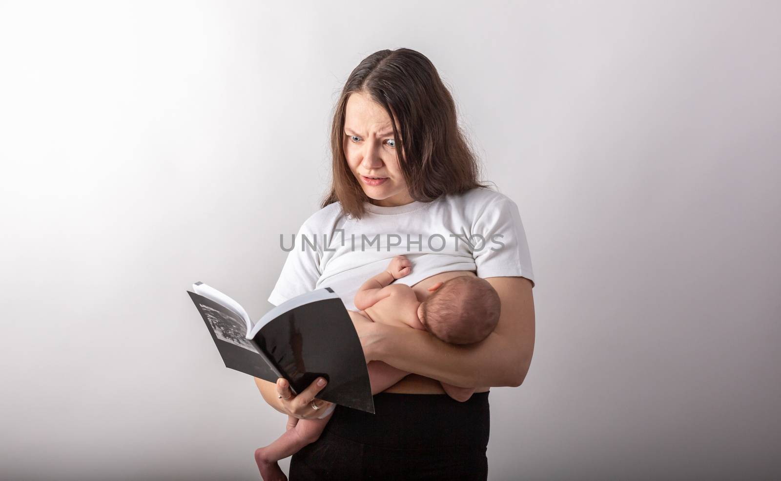 Beautiful young mother breastfeeding a baby while reading a black book.