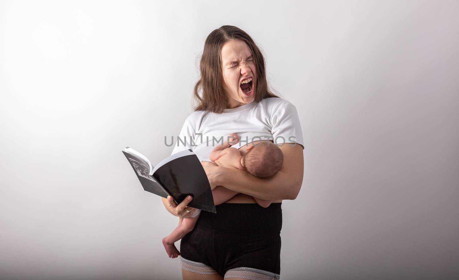 Beautiful young mother breastfeeding a baby while reading a black book by Vassiliy