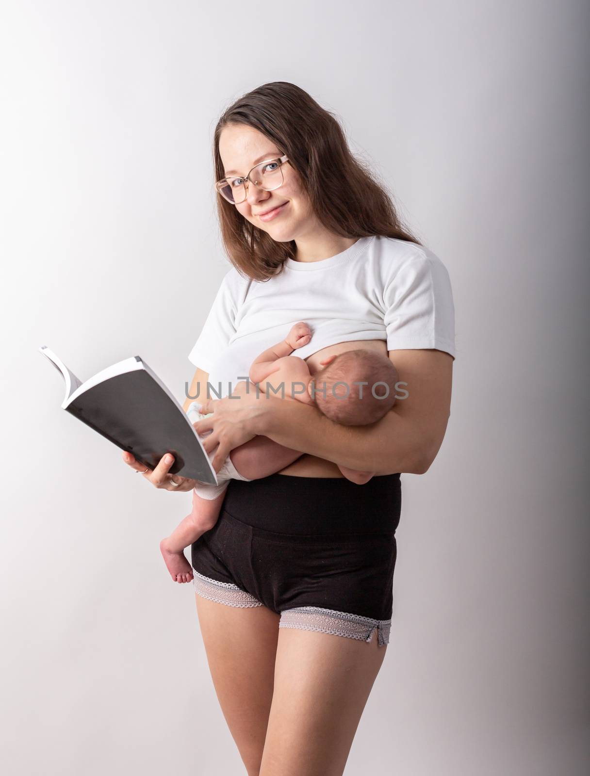 Beautiful young mother breastfeeding a baby while reading a black book.