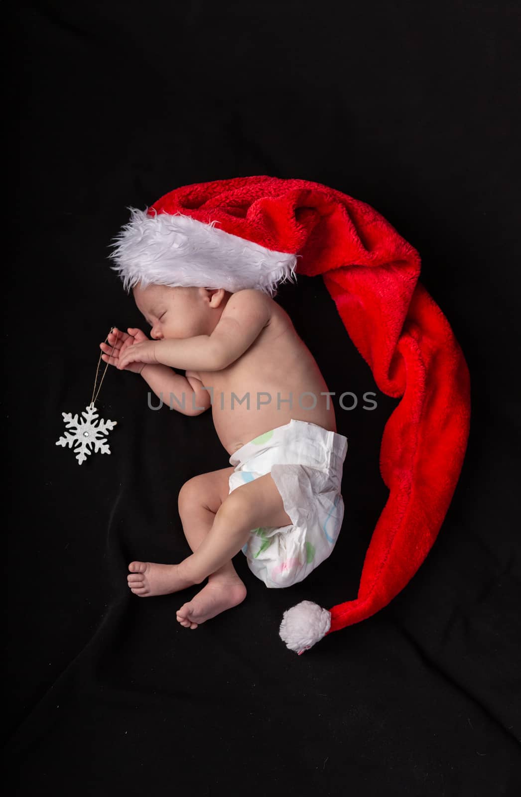 Little baby on a dark background in a long santa claus hat that lies in the shape of a crescent.