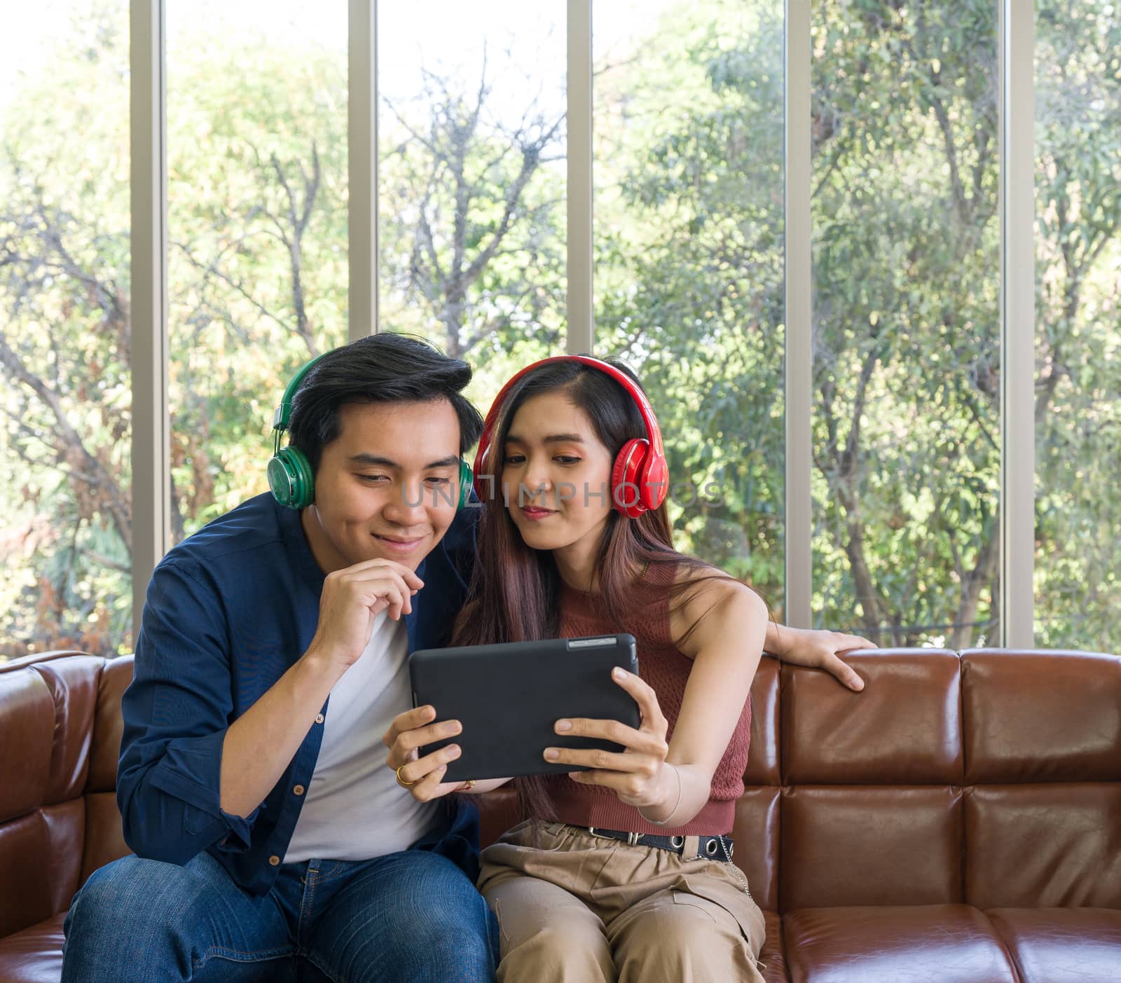 Young lovers spend time together on holidays in the living room. Both are interested in music from headphones  while the woman holding tablet computer.