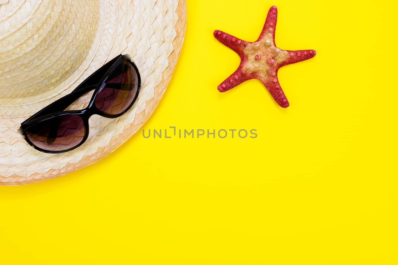 Summer holidays and vacation concept - sunglasses, starfish and a a retro beach straw on a yellow background with copy space.