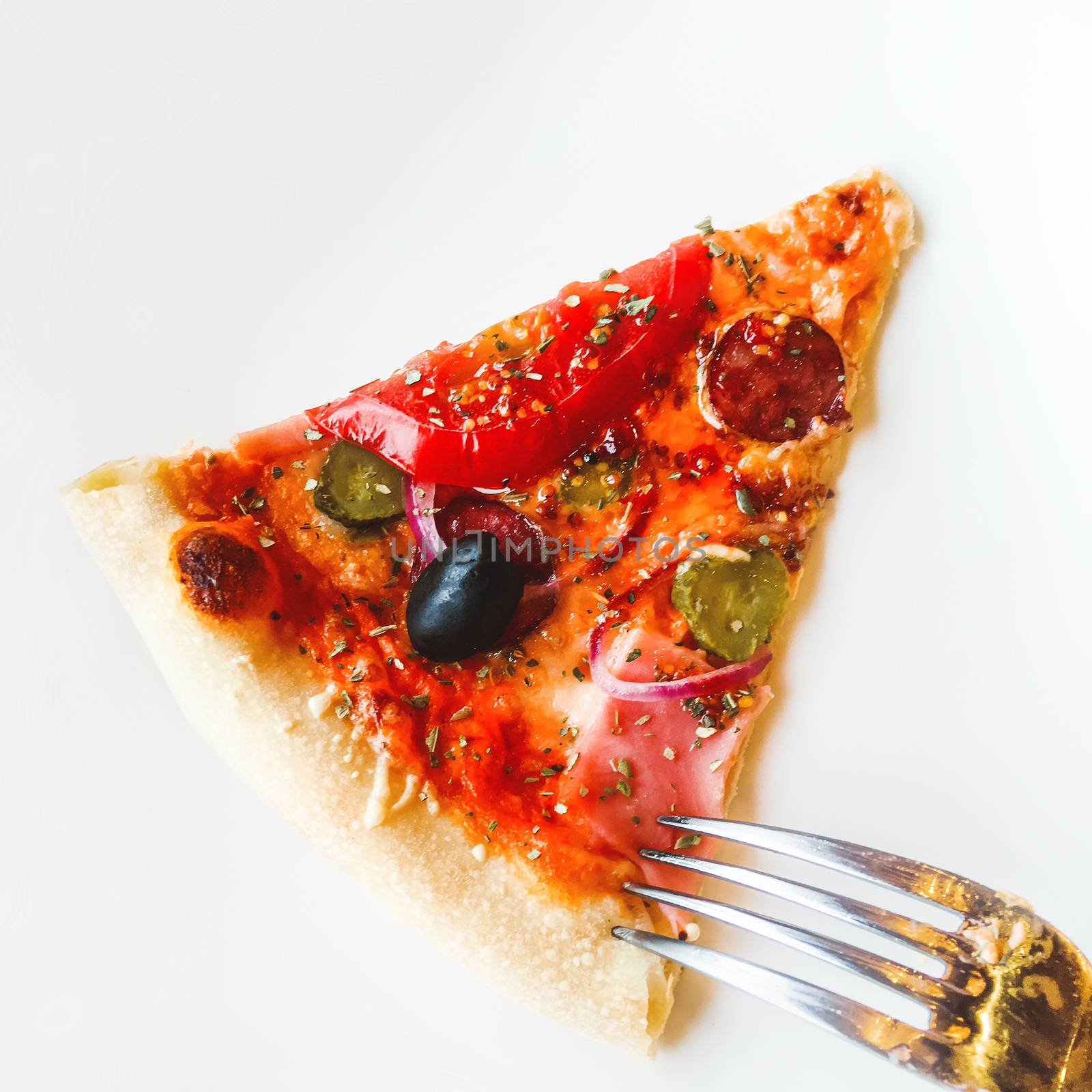 Metal fork with slice of pizza with baked ingredients - cheese with ham, marinated cucumbers, olives, tomatoes. Traditional italian cuisine. Flat lay, top view.