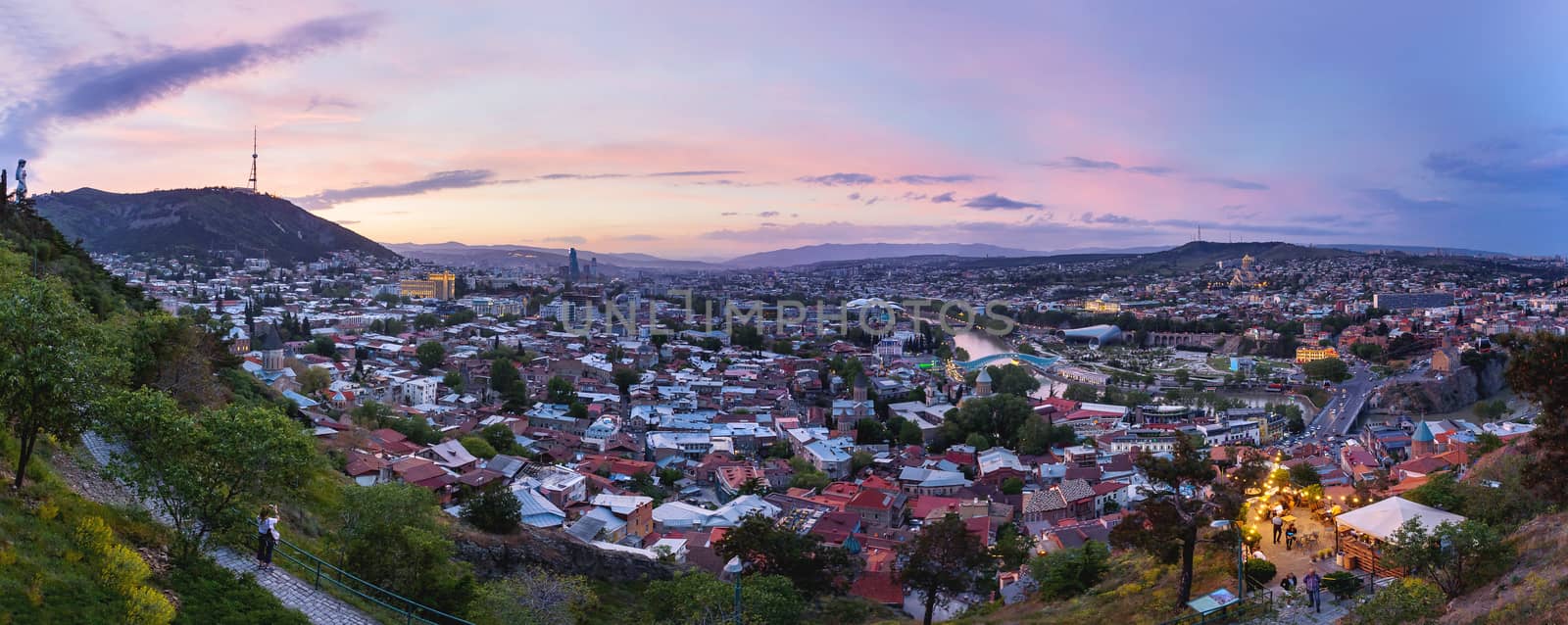 Sunset panorama view of Tbilisi, capital of Georgia country, from Narikala fortress. Famous landmarks - Metekhi church, Holy Trinity Cathedral (Sameba), Presidential Administration, Bridge of Peace with illumination. by aksenovko