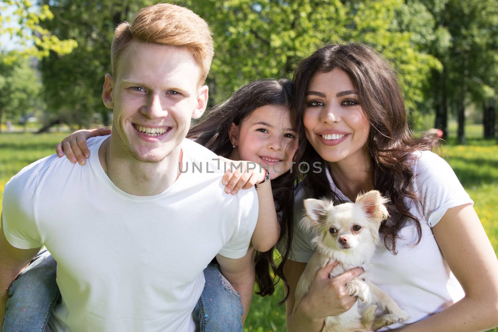 Happy smiling family of parents and daughter with pet dog in spring park