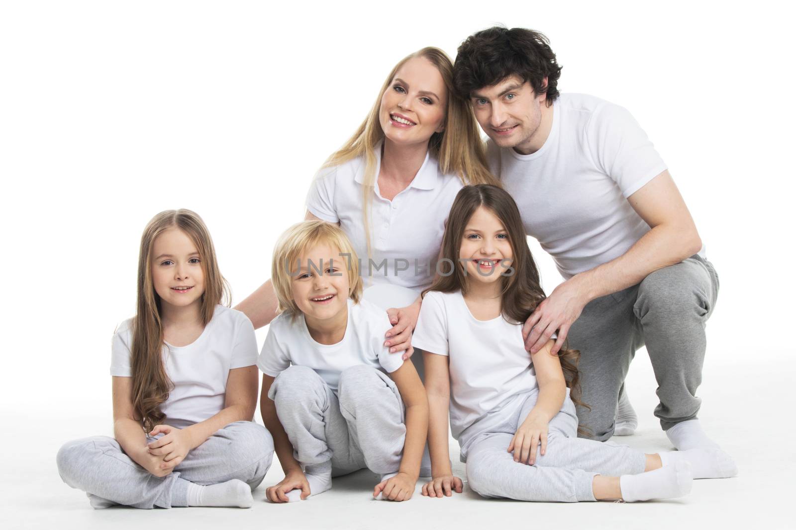 Happy smiling family of two parents and three children sitting on the floor studio isolated on white background