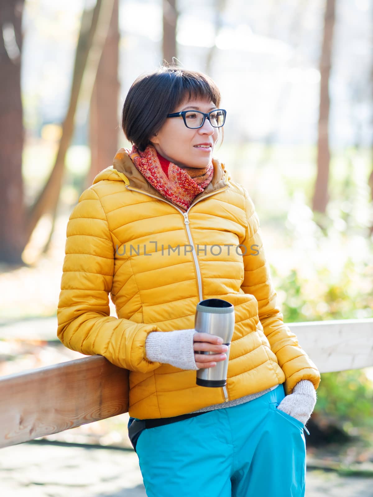 Happy wide smiling women in bright yellow jacketis holding thermos mug. Hot tea or other beverage on cool autumn day.