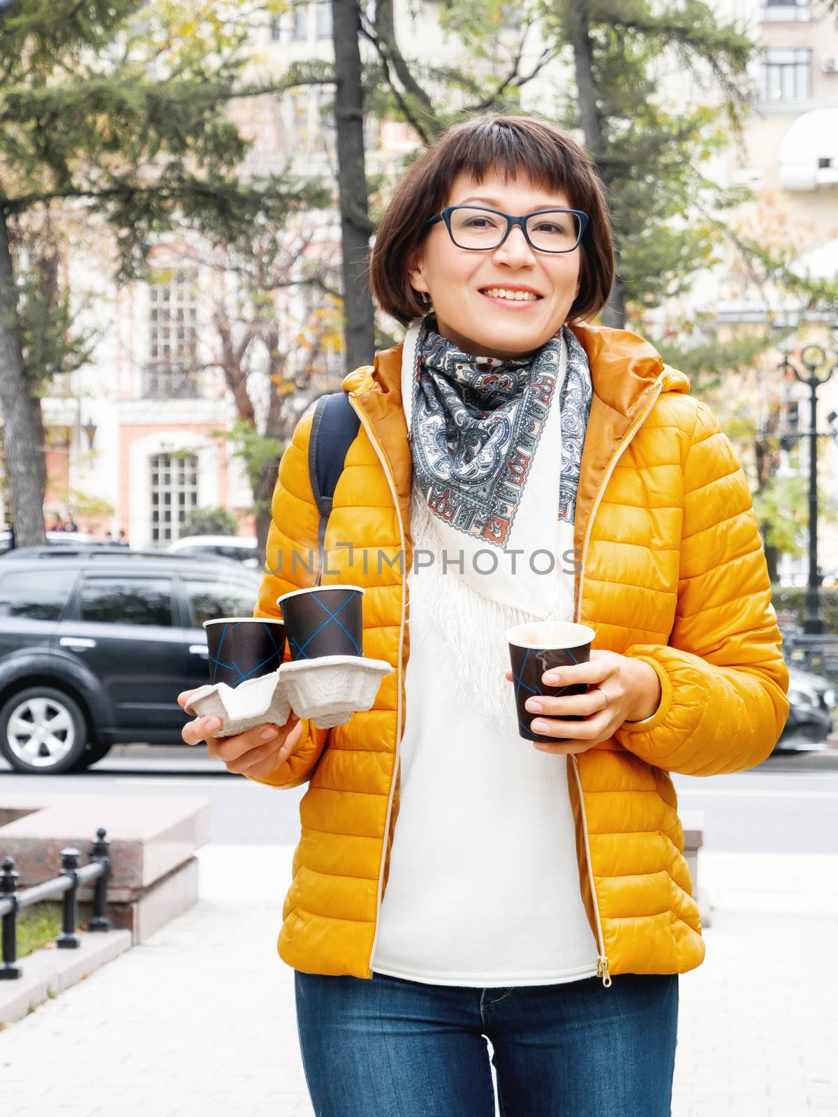 Happy wide smiling women in bright yellow jacketis holding paper cup with hot coffee. Hot beverage on cool autumn day.