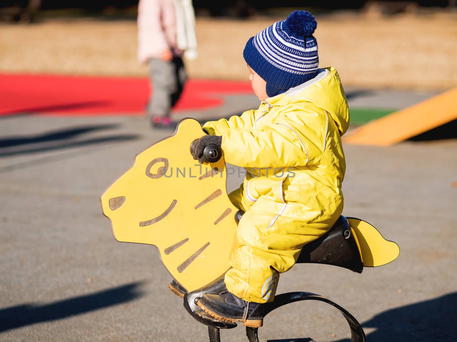 Toddler boy in yellow jumpsuit is playing on children playground. Child in bright clothes outdoor. Sunny autumn day.