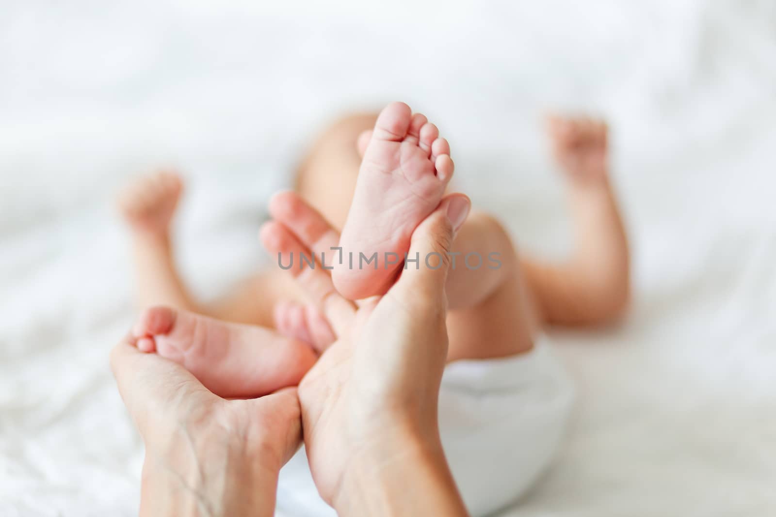 Mother holds newborn baby's bare feet. Tiny feet in woman's hand. Cozy morning at home.