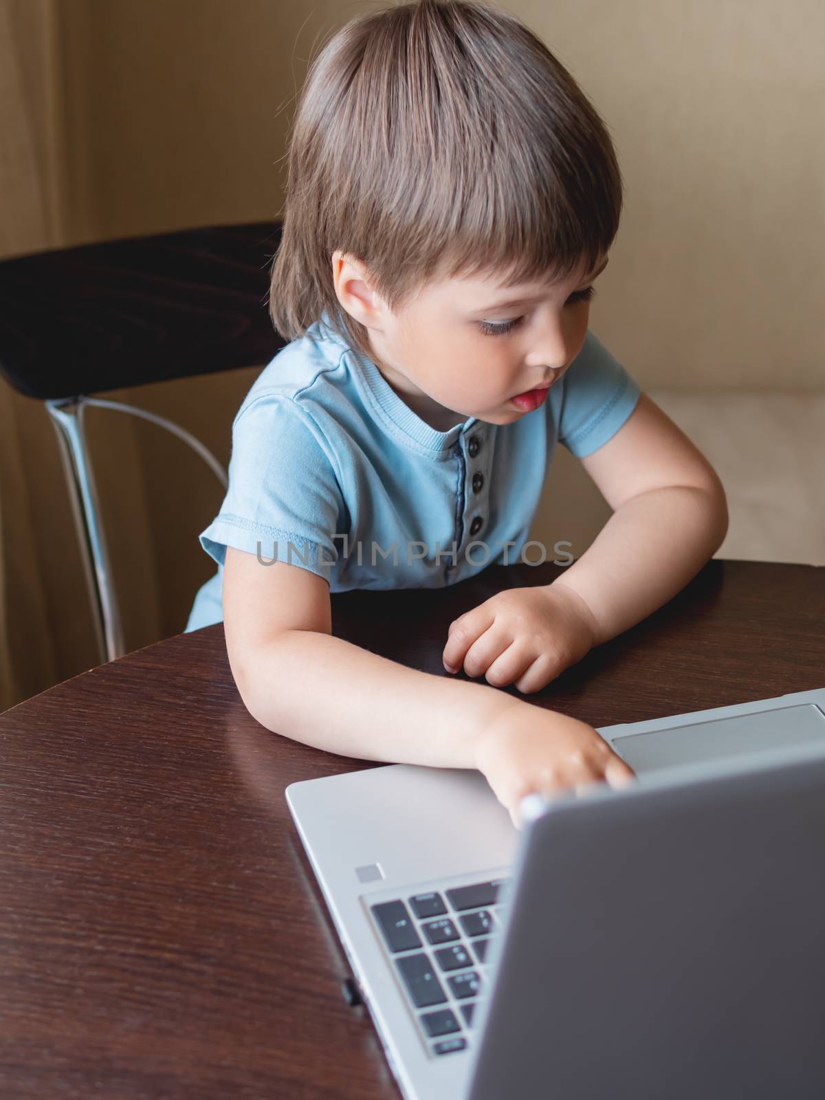 Curious toddler boy explores the laptop and presses buttons on computer keyboard.