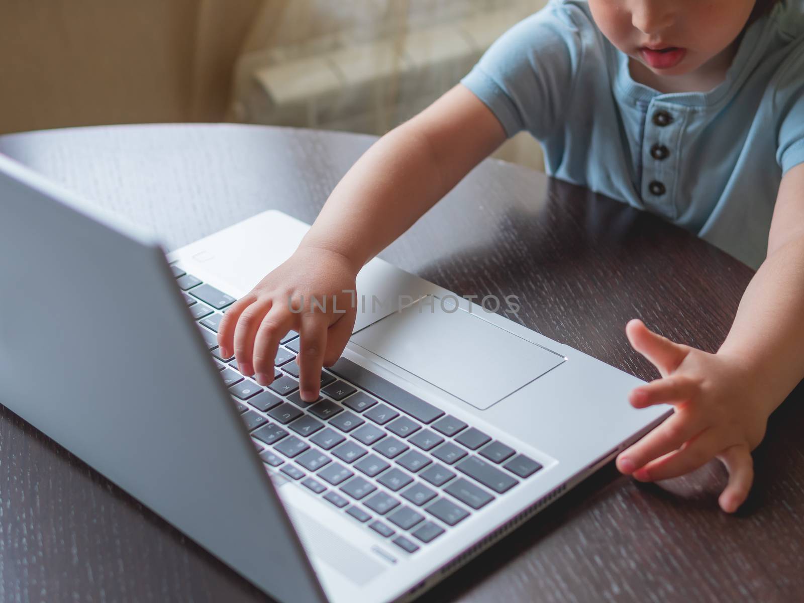 Child explores silver metal laptop. Curious toddler boy presses buttons.