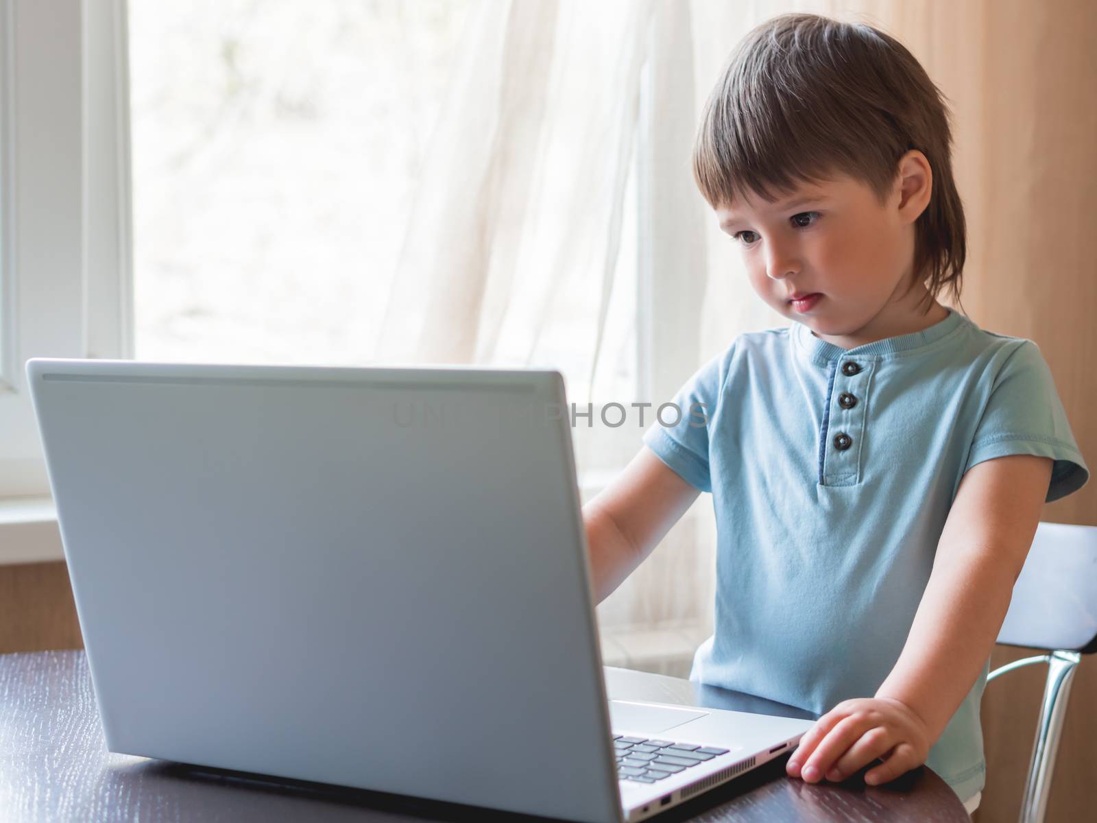 Curious toddler boy explores the laptop and presses buttons on computer keyboard.