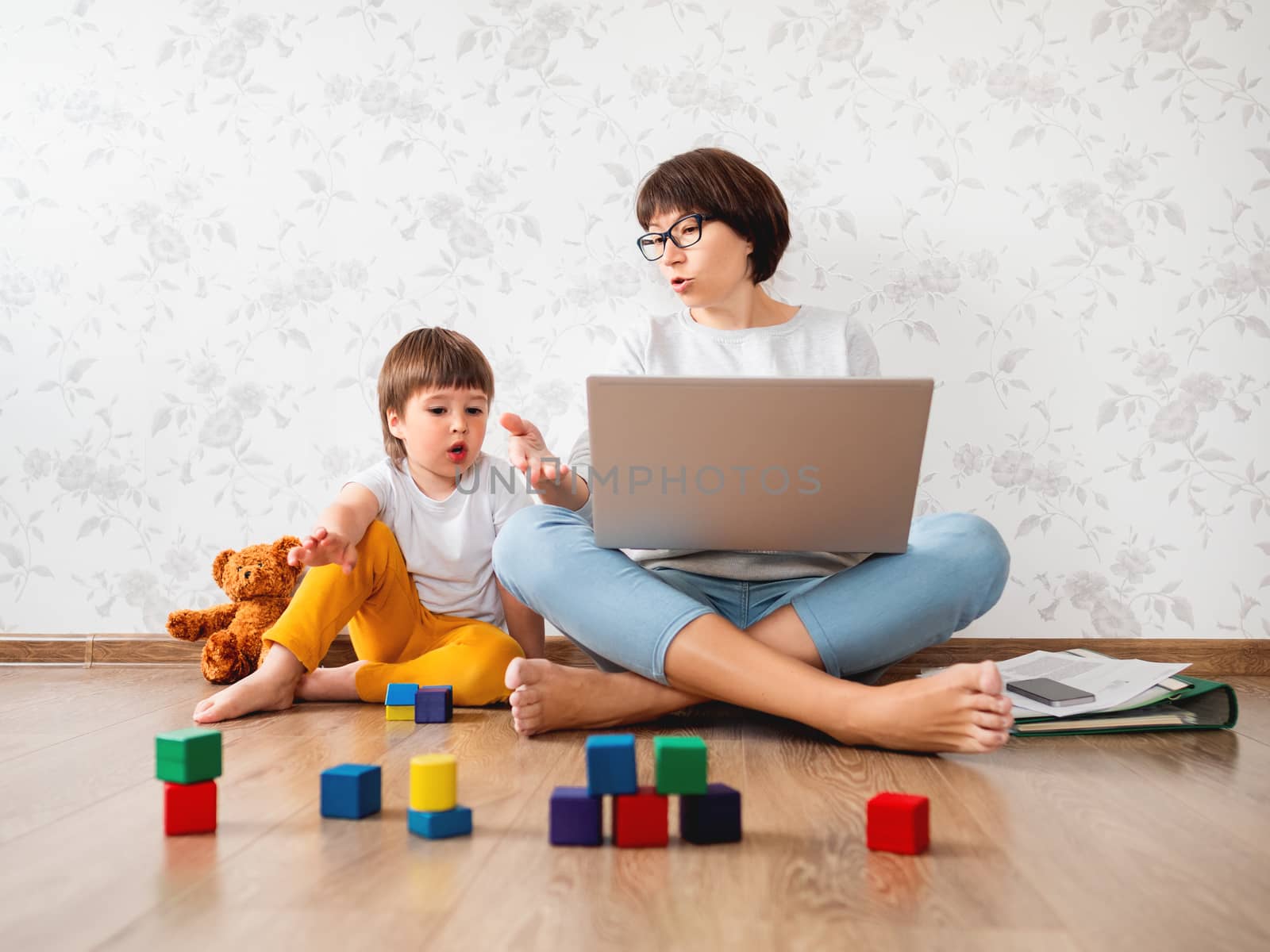 Mom and son argue at home quarantine because of coronavirus COVID19. Mother remote works with laptop, son plays with toy blocks. Self isolation at home. by aksenovko