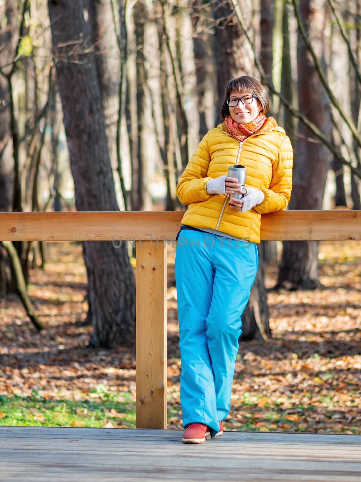 Happy wide smiling women in bright yellow jacket is holding thermos mug. Hot tea or other beverage on cool autumn day.