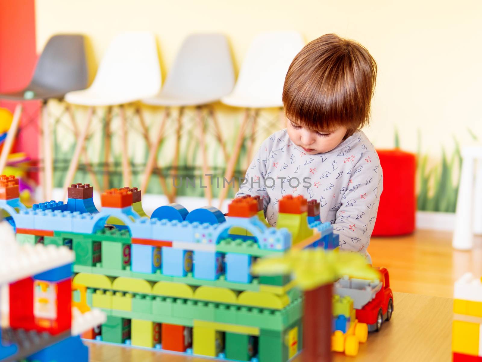 Little boy playing in nurseroom with colorful constructor. Educational toy block in toddler hands. Kid is busy with toy bricks.