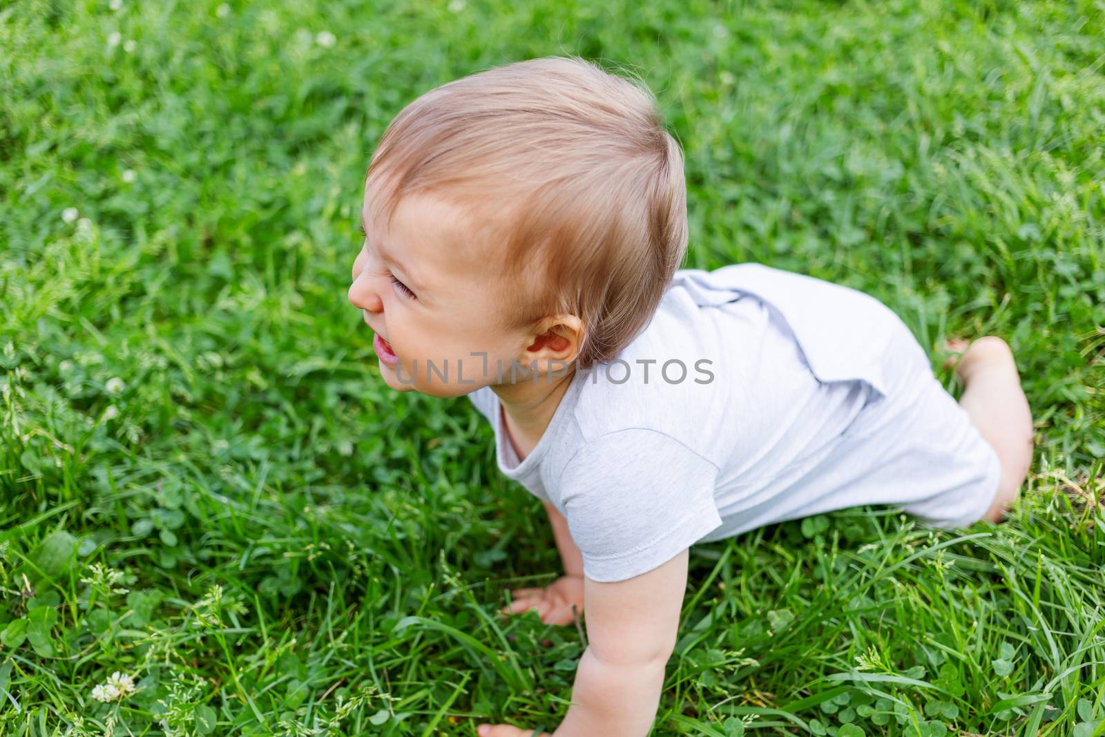 Little baby crawling on grass. Kid is laughing. Outdoor activity for kid. Natural background with child on summer lawn with fresh grass.