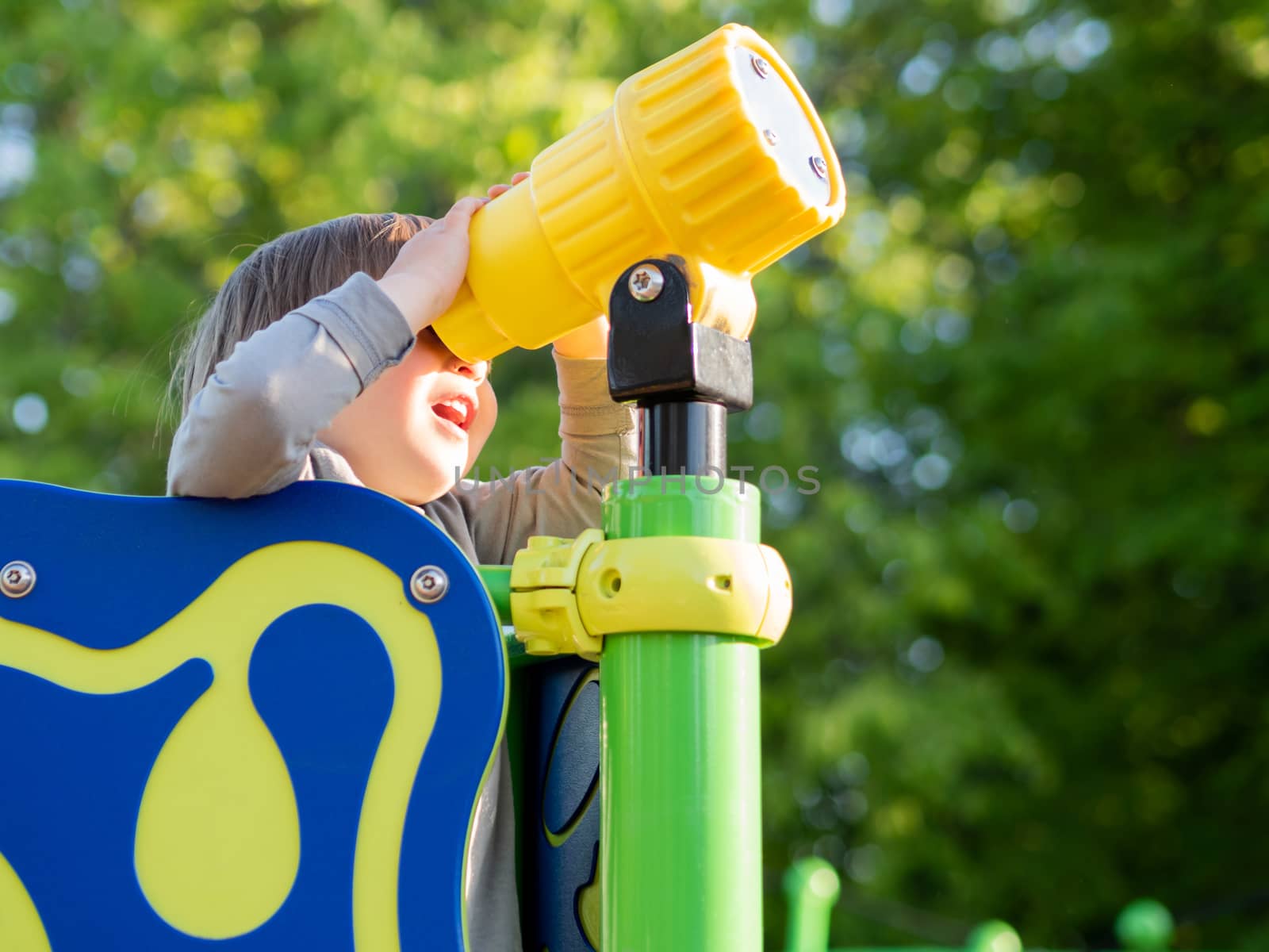 Toddler boy is playing on children playground. Child looking into a toy telescoper. Sunny summer day.