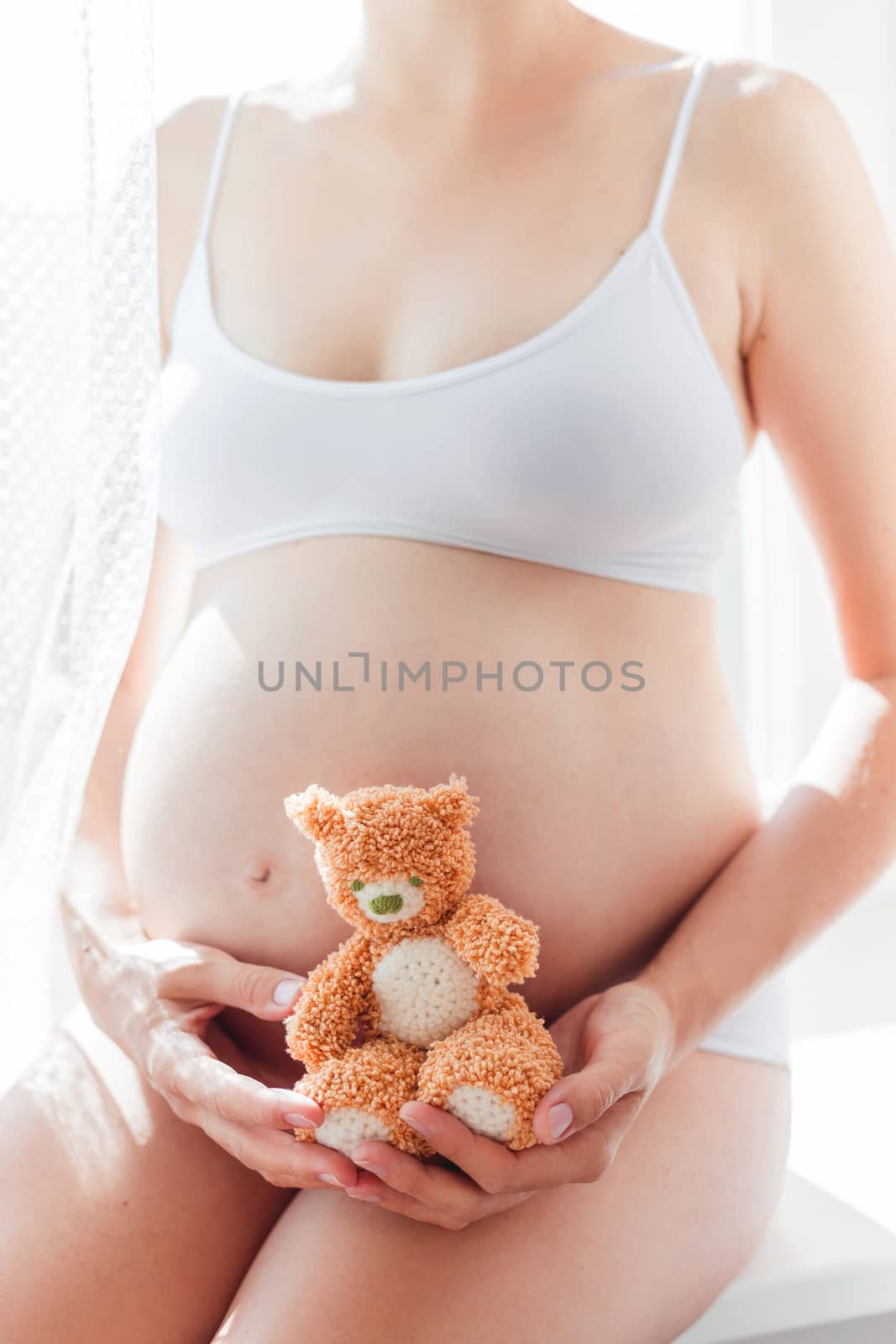 Pregnant woman in white underwear with toy bear. Young woman expecting a baby.