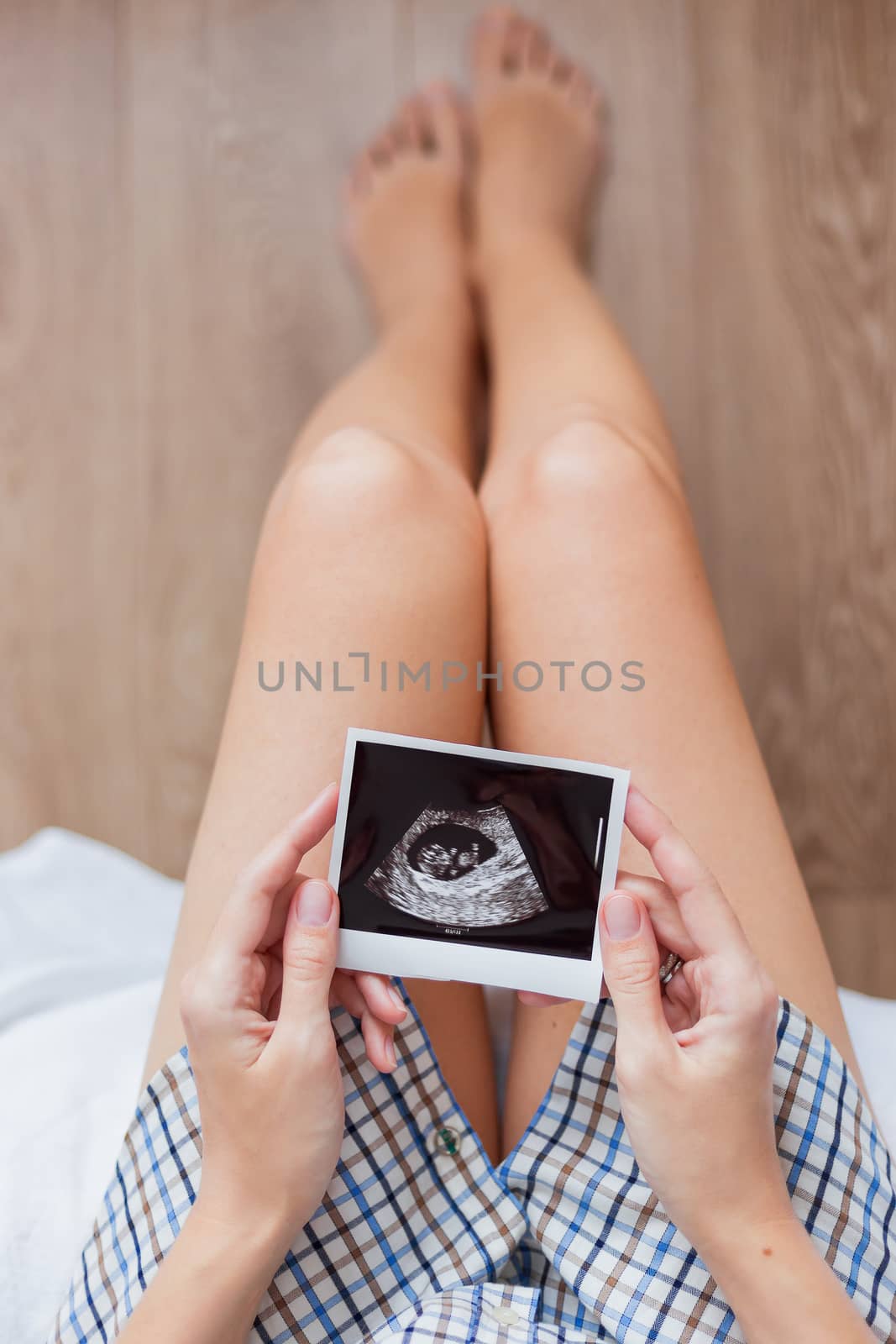 Woman in shirt sitting on bed with Ultrasound photo of baby in hands. Woman is expecting baby. Cozy happy morning at home.